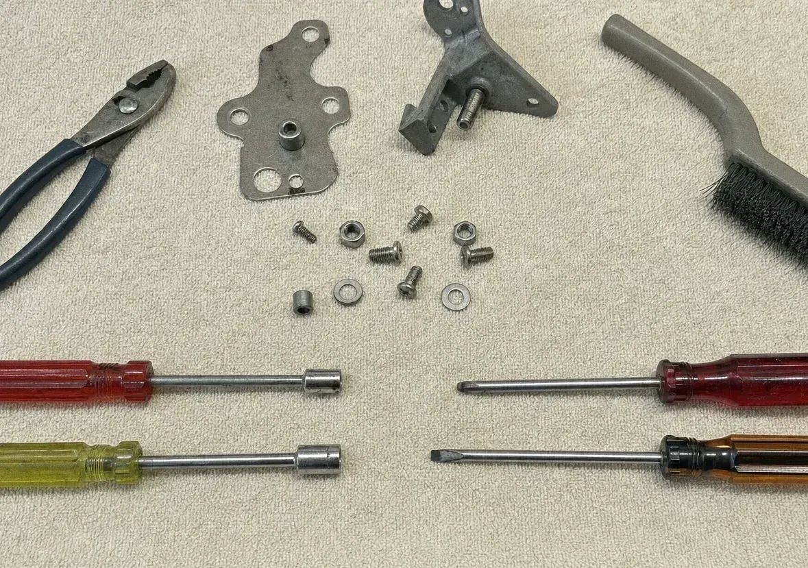 Oven door hinge plates, bolts and washers laid out beside screwdrivers, pliers and a wire brush